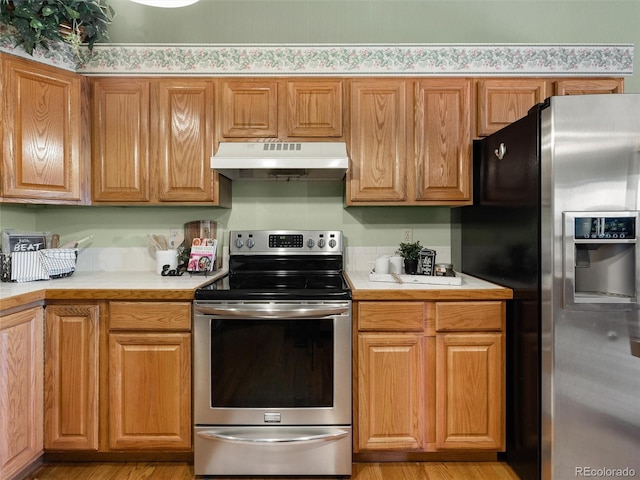 kitchen featuring brown cabinetry, stainless steel appliances, light countertops, light wood-type flooring, and under cabinet range hood