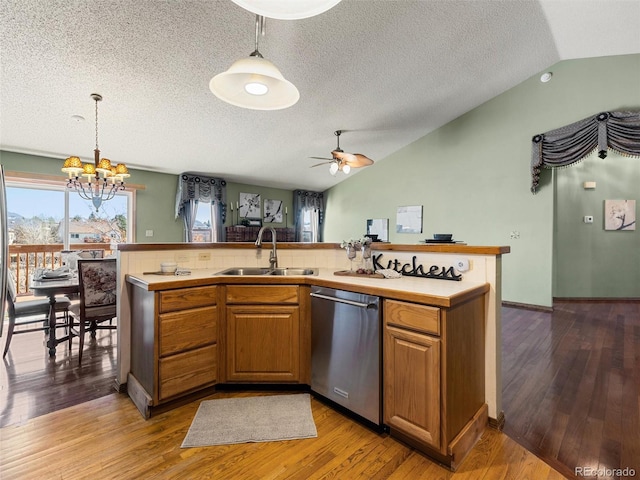 kitchen with light countertops, stainless steel dishwasher, vaulted ceiling, a sink, and light wood-type flooring