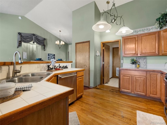 kitchen with tile countertops, stainless steel dishwasher, light wood-style floors, vaulted ceiling, and a sink