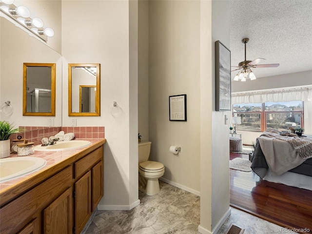 full bath featuring double vanity, toilet, connected bathroom, a textured ceiling, and a sink