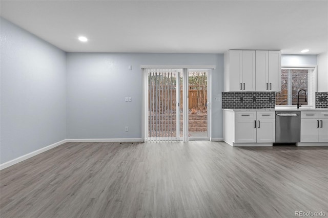 kitchen featuring light wood-style flooring, baseboards, light countertops, dishwasher, and tasteful backsplash