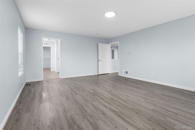 empty room with wood finished floors, visible vents, and baseboards