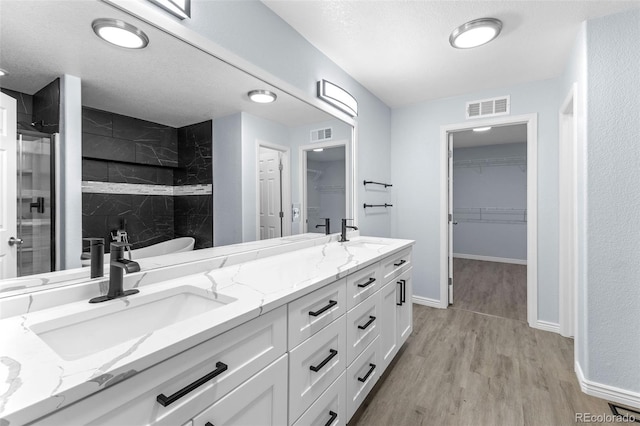 full bath with a shower stall, visible vents, a sink, and wood finished floors