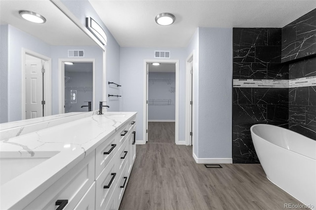 full bathroom featuring a freestanding tub, visible vents, double vanity, and wood finished floors