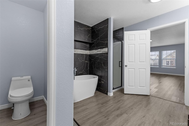 bathroom featuring a freestanding tub, a stall shower, wood finished floors, and toilet