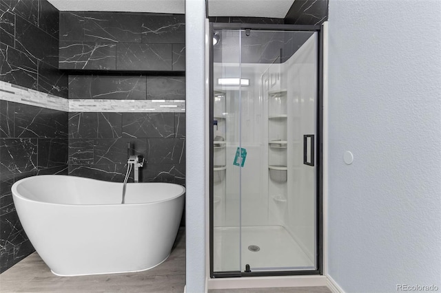 full bath featuring a freestanding tub, a shower stall, wood finished floors, and a textured wall