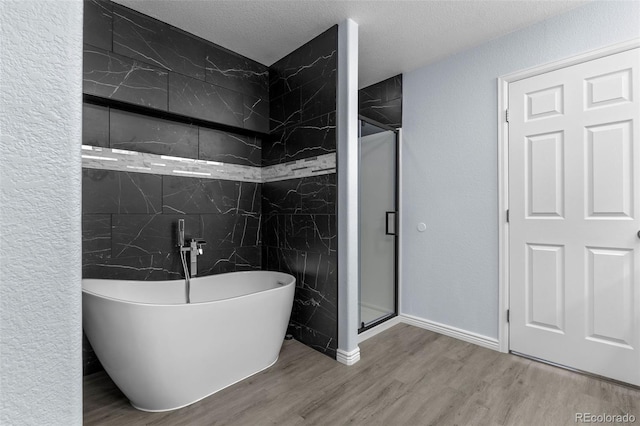 bathroom featuring a textured ceiling, a stall shower, a soaking tub, and wood finished floors