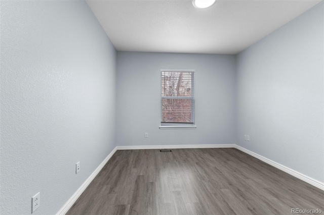 empty room with dark wood-style flooring, visible vents, and baseboards