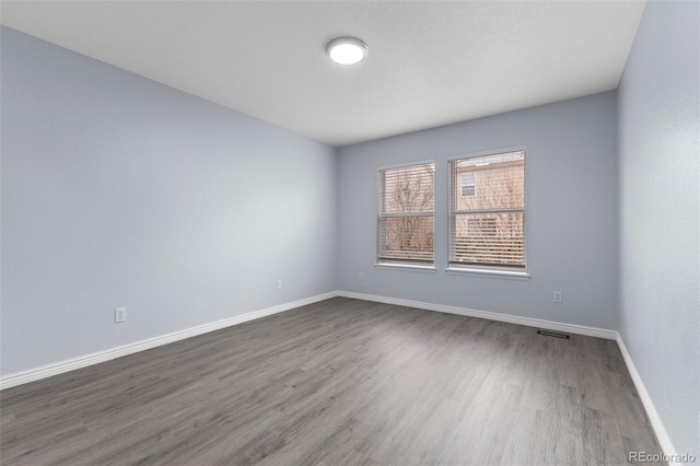 spare room featuring dark wood-style flooring, visible vents, and baseboards