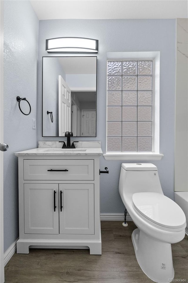 bathroom featuring toilet, baseboards, wood finished floors, and vanity