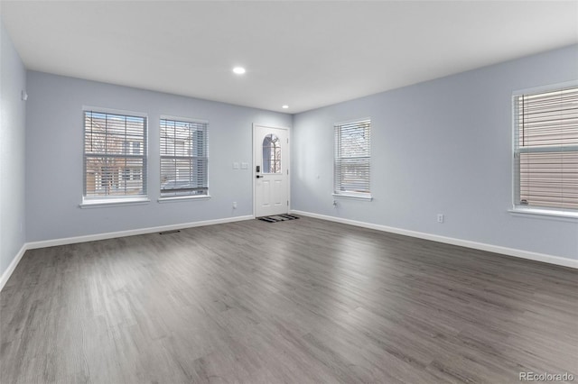 empty room with a healthy amount of sunlight, baseboards, dark wood finished floors, and recessed lighting