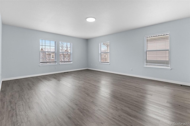 unfurnished room featuring dark wood-style floors, visible vents, and baseboards