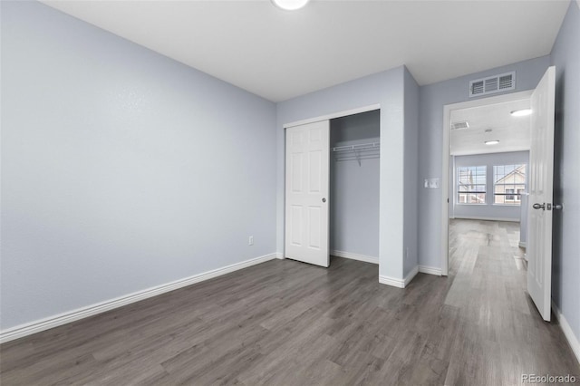 unfurnished bedroom featuring dark wood-style floors, baseboards, visible vents, and a closet