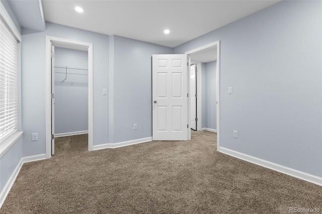 unfurnished bedroom with carpet, a spacious closet, baseboards, and multiple windows