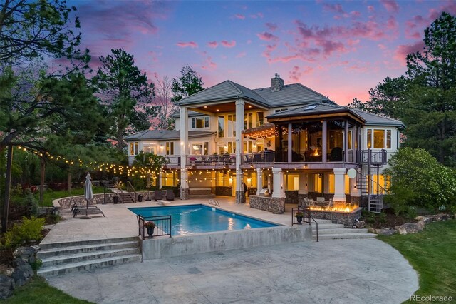 10914 Remmick Ridge Rd, Parker, CO 80134 - back of property at dusk with stairs, a balcony, a chimney, a patio, and an outdoor pool
