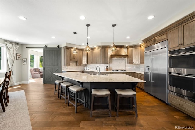 10914 Remmick Ridge Rd, Parker, CO 80134 - kitchen with appliances with stainless steel finishes, custom exhaust hood, a sink, a barn door, and backsplash