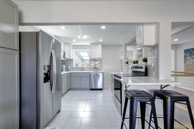 kitchen featuring gray cabinetry, backsplash, sink, a kitchen bar, and stainless steel appliances