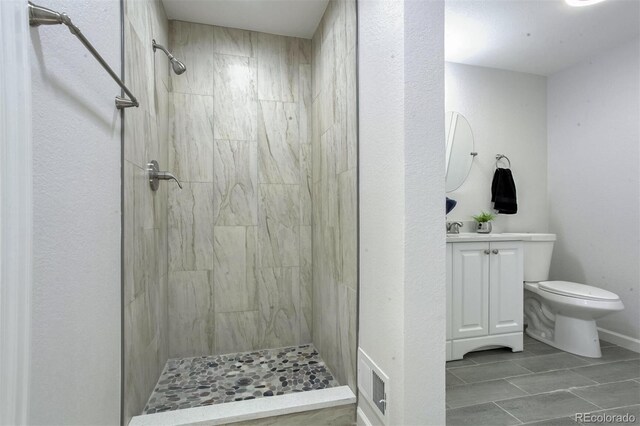 bathroom with a tile shower, vanity, and toilet