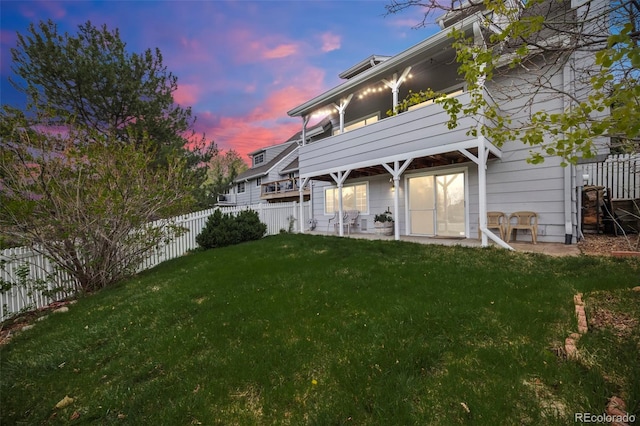 back of house at dusk with a yard, a fenced backyard, and a balcony