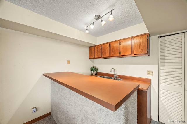 kitchen featuring brown cabinetry, a peninsula, carpet flooring, a textured ceiling, and a sink