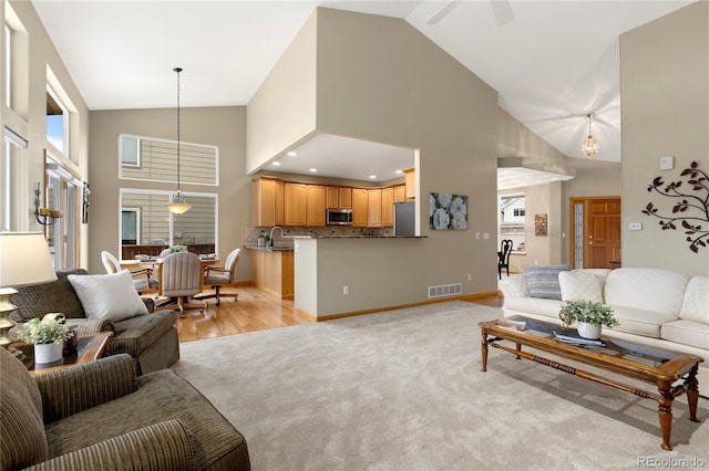 living area featuring light colored carpet, baseboards, visible vents, and high vaulted ceiling