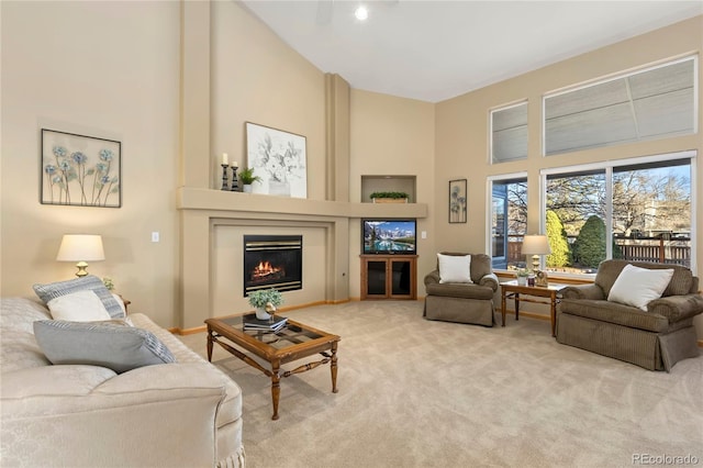 living area with a glass covered fireplace, light carpet, and a towering ceiling