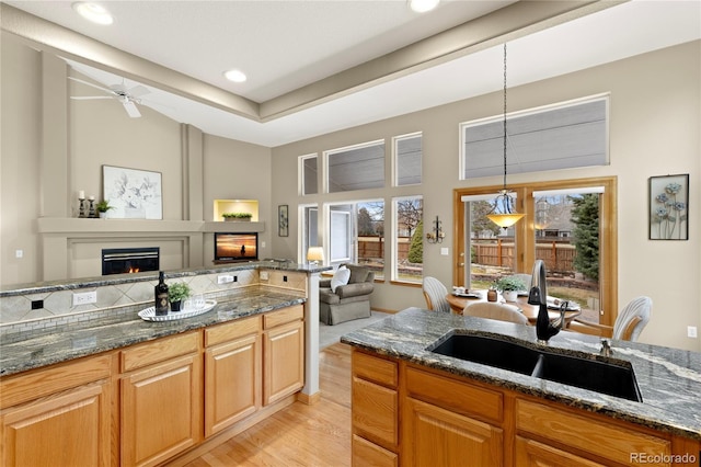 kitchen featuring a glass covered fireplace, dark stone countertops, open floor plan, and a sink