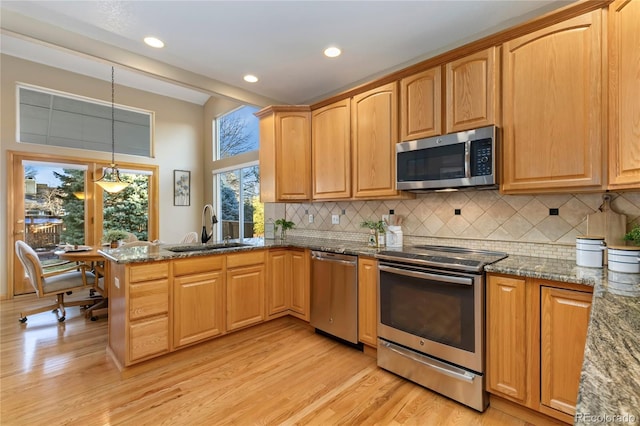 kitchen with dark stone countertops, a peninsula, a sink, stainless steel appliances, and light wood-type flooring