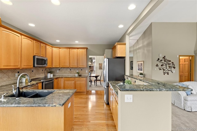 kitchen featuring a sink, dark stone countertops, appliances with stainless steel finishes, a peninsula, and light wood finished floors