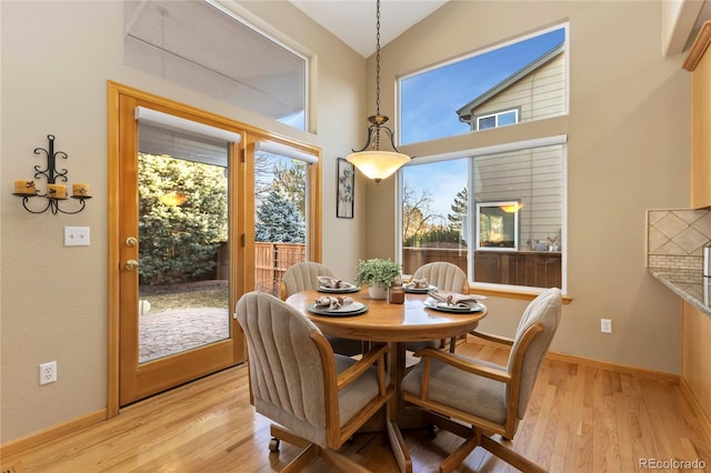 dining room with light wood-style flooring, baseboards, and high vaulted ceiling