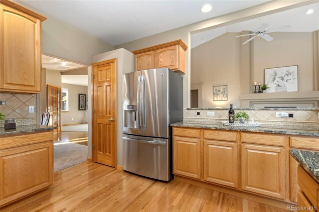 kitchen with light wood-type flooring, dark stone countertops, tasteful backsplash, stainless steel fridge, and lofted ceiling