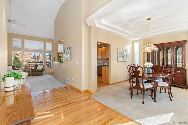 dining room featuring baseboards, visible vents, a raised ceiling, ceiling fan with notable chandelier, and light wood-type flooring