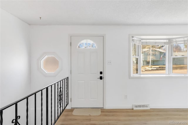 foyer entrance with wood finished floors, a healthy amount of sunlight, visible vents, and a textured ceiling