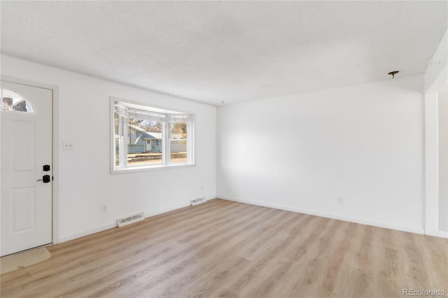 foyer entrance featuring visible vents, a textured ceiling, light wood-type flooring, and baseboards