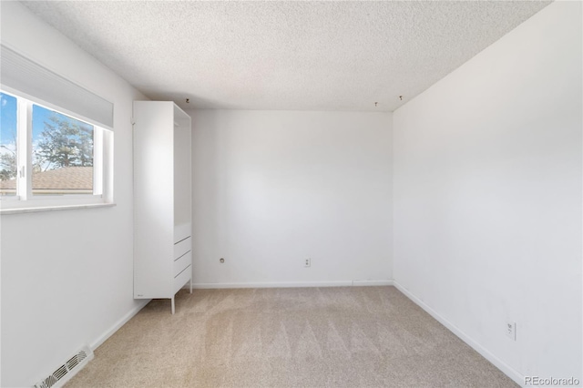 spare room featuring a textured ceiling, baseboards, visible vents, and light carpet