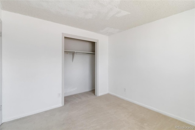 unfurnished bedroom featuring a textured ceiling, baseboards, a closet, and light carpet