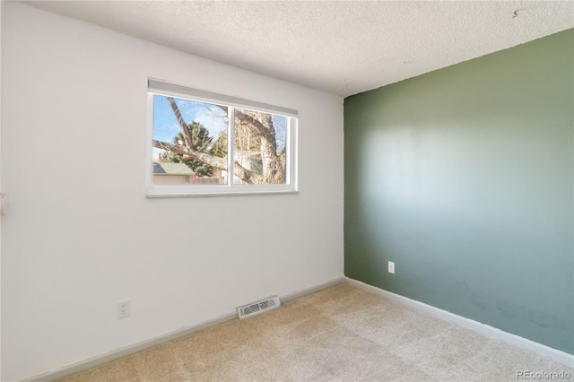 carpeted spare room with visible vents, baseboards, and a textured ceiling