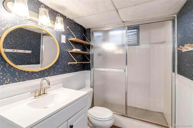 full bathroom with wallpapered walls, toilet, a stall shower, vanity, and a paneled ceiling