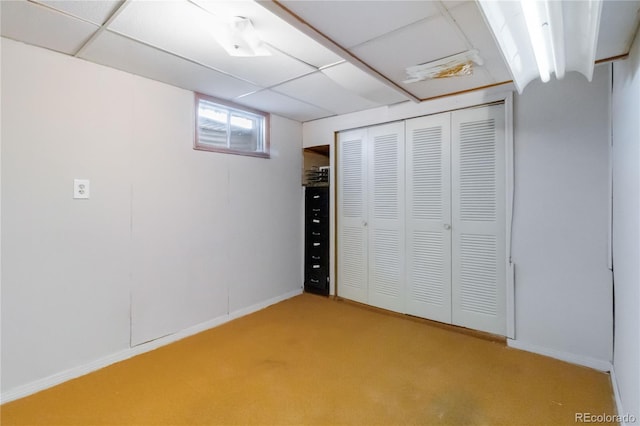 unfurnished bedroom with baseboards, a closet, a paneled ceiling, and light carpet