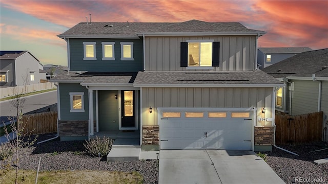 view of front of home with board and batten siding, fence, stone siding, and concrete driveway