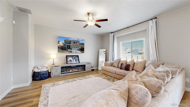 living room with a ceiling fan, wood finished floors, baseboards, and a glass covered fireplace