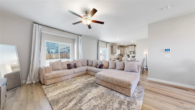 living room featuring ceiling fan, light wood-type flooring, and baseboards