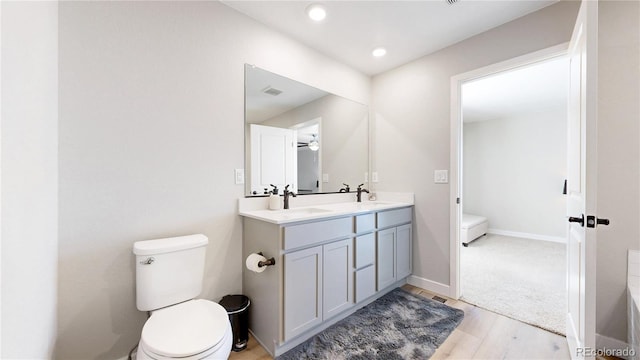 bathroom featuring toilet, wood finished floors, double vanity, ceiling fan, and baseboards