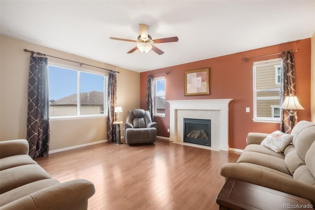 living room featuring a ceiling fan, wood finished floors, a fireplace with flush hearth, and baseboards