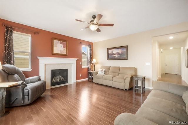 living area featuring ceiling fan, wood finished floors, a glass covered fireplace, and baseboards