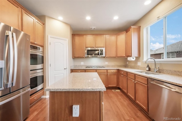 kitchen with stainless steel appliances, a sink, light wood-type flooring, a center island, and light stone counters