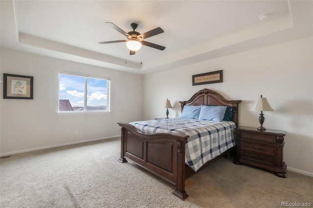 bedroom with a raised ceiling, light colored carpet, baseboards, and ceiling fan
