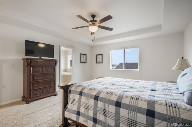 bedroom featuring light carpet, a raised ceiling, a ceiling fan, baseboards, and ensuite bath