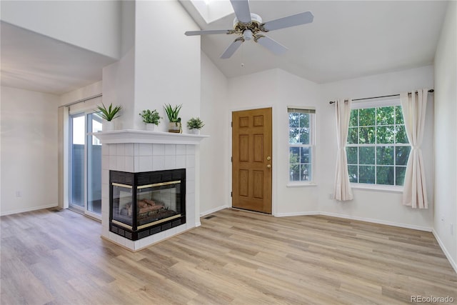 unfurnished living room with a tile fireplace, lofted ceiling, ceiling fan, and light wood-type flooring