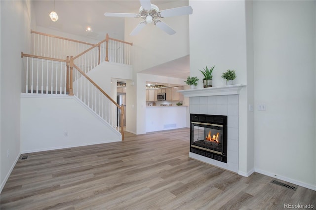 unfurnished living room with a high ceiling, a tile fireplace, ceiling fan, and light wood-type flooring